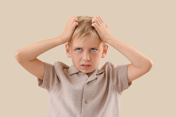 Upset little boy with pediculosis scratching his head on beige background