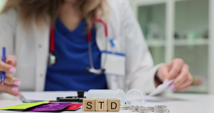 Abbreviation STD on wooden cubes and condoms against doctor writing on clipboard in hospital. Sexually transmitted disease awareness