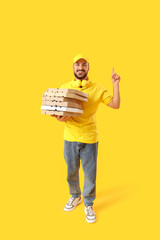 Male courier with pizza boxes pointing at something on  yellow background