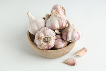 Wooden bowl with fresh garlic and cloves on white background