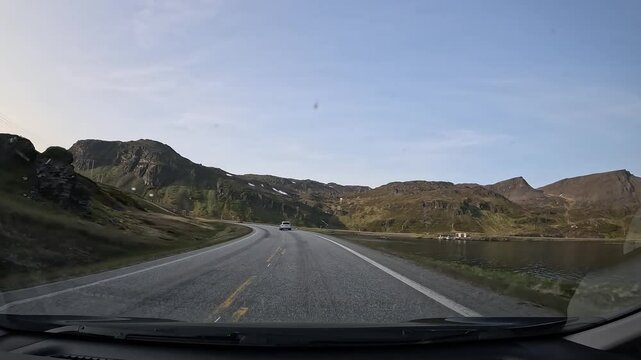 Driving through the tundra of northern Norway on E69 road. Rocky hills with grass surround the area, with the sea visible on the right side.