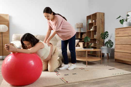 Young Asian doula and pregnant woman training with fitball at home