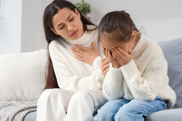 Mother apologizing to her crying daughter on sofa at home
