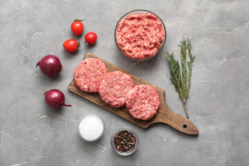 Cutting board with raw meat cutlets and rosemary on grey grunge background