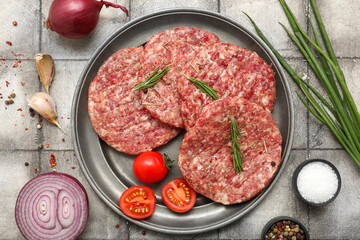 Plate with raw meat cutlets on grey tile background