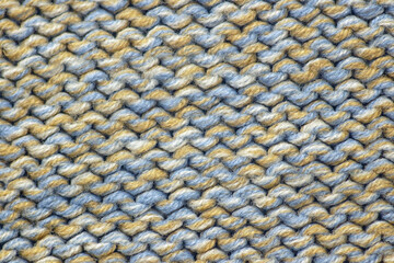 Background of knitting patterns. A close-up photo from above of the rows of a warm sweater made using the garter stitch technique and thick multi-colored yarn. Fabric texture: woolen cloth.