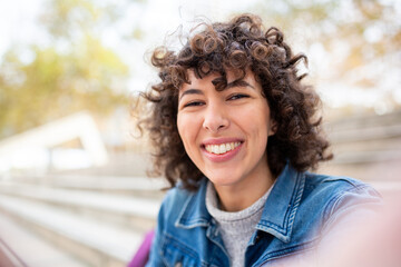 Close-up portrait of a young smiling woman in a denim jacket outdoors