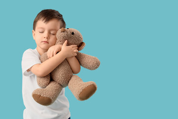 Cute little boy hugging toy bear on blue background