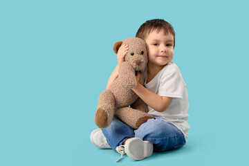 Cute little boy hugging toy bear on blue background