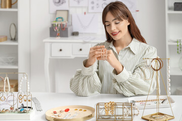 Young female jewelry designer with bracelet at table in workshop