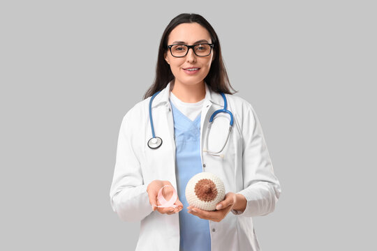 Female doctor with pink awareness ribbon and knitted breast model on light background