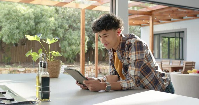 Smiling young man using tablet while leaning on kitchen counter at home