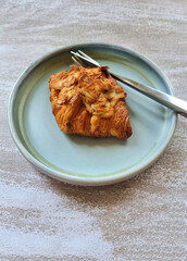 Vertical shot of the croissant is on at the plate with spoon and fork.