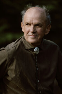 Close-up of elderly man in bolo tie, gazing thoughtfully outdoors.