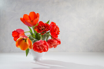 A bouquet of red tulips in a white vase on a light background. Copy space