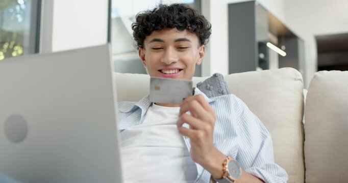 Shopping online, smiling teenage boy holding credit card and using laptop on couch