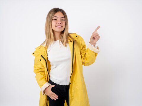 Beautiful teen girl wearing rain coat looking at camera indicating finger empty space sales