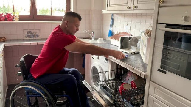 handicapped man in wheelchair puts dishes in a dishwasher, do kitchen work independently