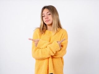 Beautiful caucasian teen girl wearing orange sweater points away and gives advice demonstrates advertisement