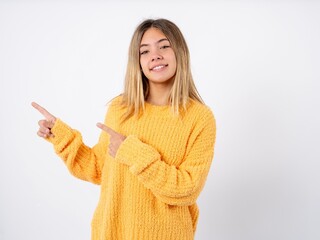 Beautiful caucasian teen girl wearing orange sweater points aside on copy blank space. People promotion and advertising concept