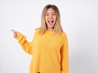 Beautiful caucasian teen girl wearing orange sweater points at copy space and advertises something, advices best price.