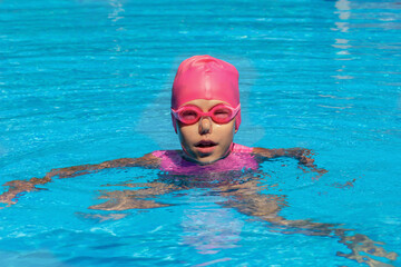 Child in swimming cap, goggles and nose clip in swimming pool