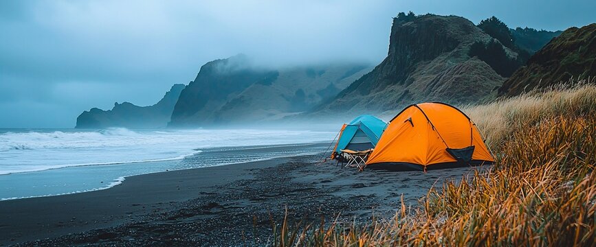 Two tents on a beach with dramatic cliffs and ocean waves under a cloudy sky.