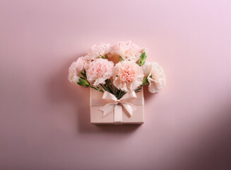 A delicate bouquet of light pink carnations nestled in a pale pink gift box, tied with a satin ribbon.  The arrangement sits against a matching pastel background.