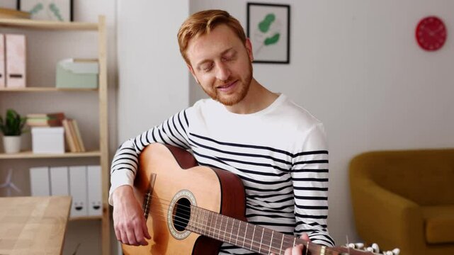 Man learning guitar in online music class with distant teacher on computer from home - Young adult teaching music through laptop. Distance education learning concept