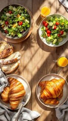 Breakfast spread with croissants, fresh salads, bread, and orange juice on wooden table