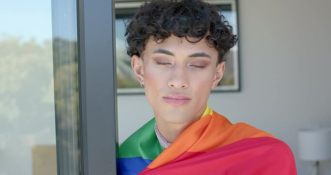 Wearing pride flag, non binary person standing by window, looking confident