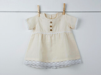 Beige baby dress with lace accents and wooden buttons hanging on a clothesline, showcasing a...