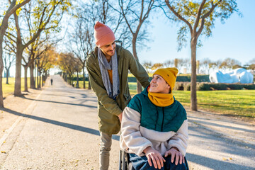 Young man pushing friend in wheelchair in a park during fall season