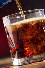 Cola is poured into a glass with ice cubes on a dark background close-up
