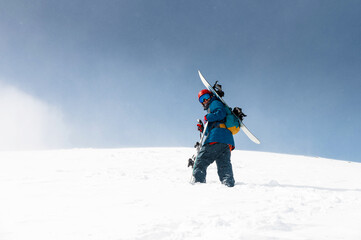 Young man in mountains ready to go snowboarding. Man carrying sports equipment climbing mountain in...