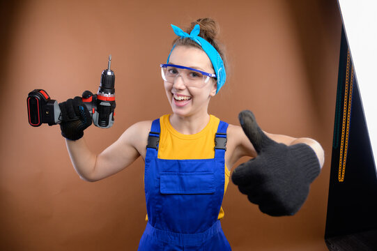 Caucasian female construction worker showing thumb up at final stage of site reconstruction. Happy white young woman worker in safety glasses and gloves with close-up gesture of admiration