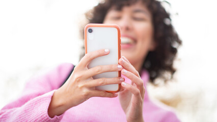Close-up of a woman with curly hair holding a smartphone with two hands outdoors
