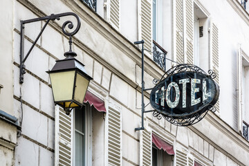 The worn period sign of a modest hotel, made of wrought iron and glass, fixed perpendicularly to the facade of an old building next to a vintage street light in a touristic district of Paris, France.