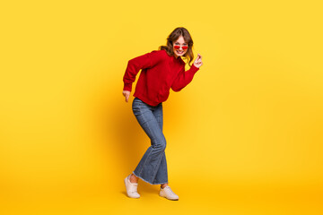 Fototapeta premium Cheerful young woman in trendy red sweater dancing against a vibrant yellow background, showcasing stylish casual wear