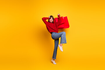 Joyful young woman posing cheerfully with shopping bags on vibrant yellow background