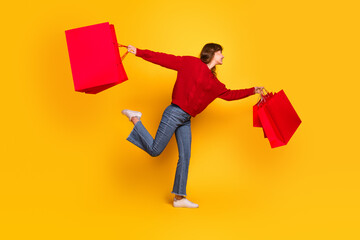 Young woman in red sweater holding shopping bags while posing playfully against vibrant yellow...