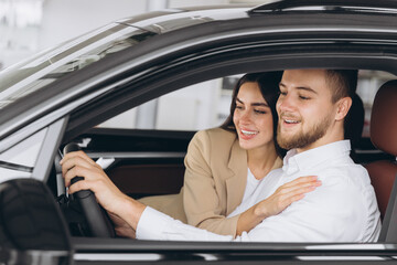 Portrait of smiling beautiful couple sitting in modern luxury car, happy excited young man and woman buying new car in dealership.