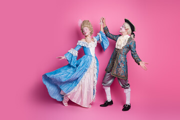 Fototapeta premium A couple in elaborate baroque costumes posed gracefully against a vibrant pink backdrop