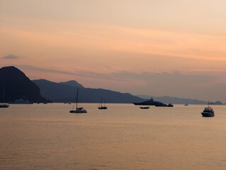 Serene Sunset View of Yachts and Boats on Calm Waters with Mountain Backdrop
