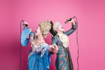 Elegant couple in vintage costumes singing joyfully against a vibrant pink background. Baroque...