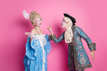 Elegant couple in baroque era costumes against pink background evokes historical romance and...