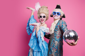 Energetic couple in baroque costumes poses joyfully against a vibrant pink background, capturing...