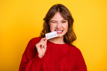 Charming woman with a cheerful expression holding a credit card on a yellow background