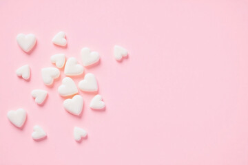 Small heart shaped candies of white and pink scatter on pink