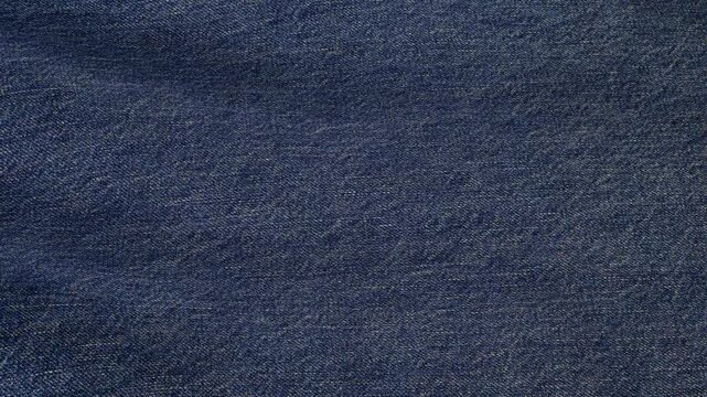 Smooth soft denim fabric textures flow in waves, highlighting refined luxurious patterns with exclusive tactile richness and elegant premium design
